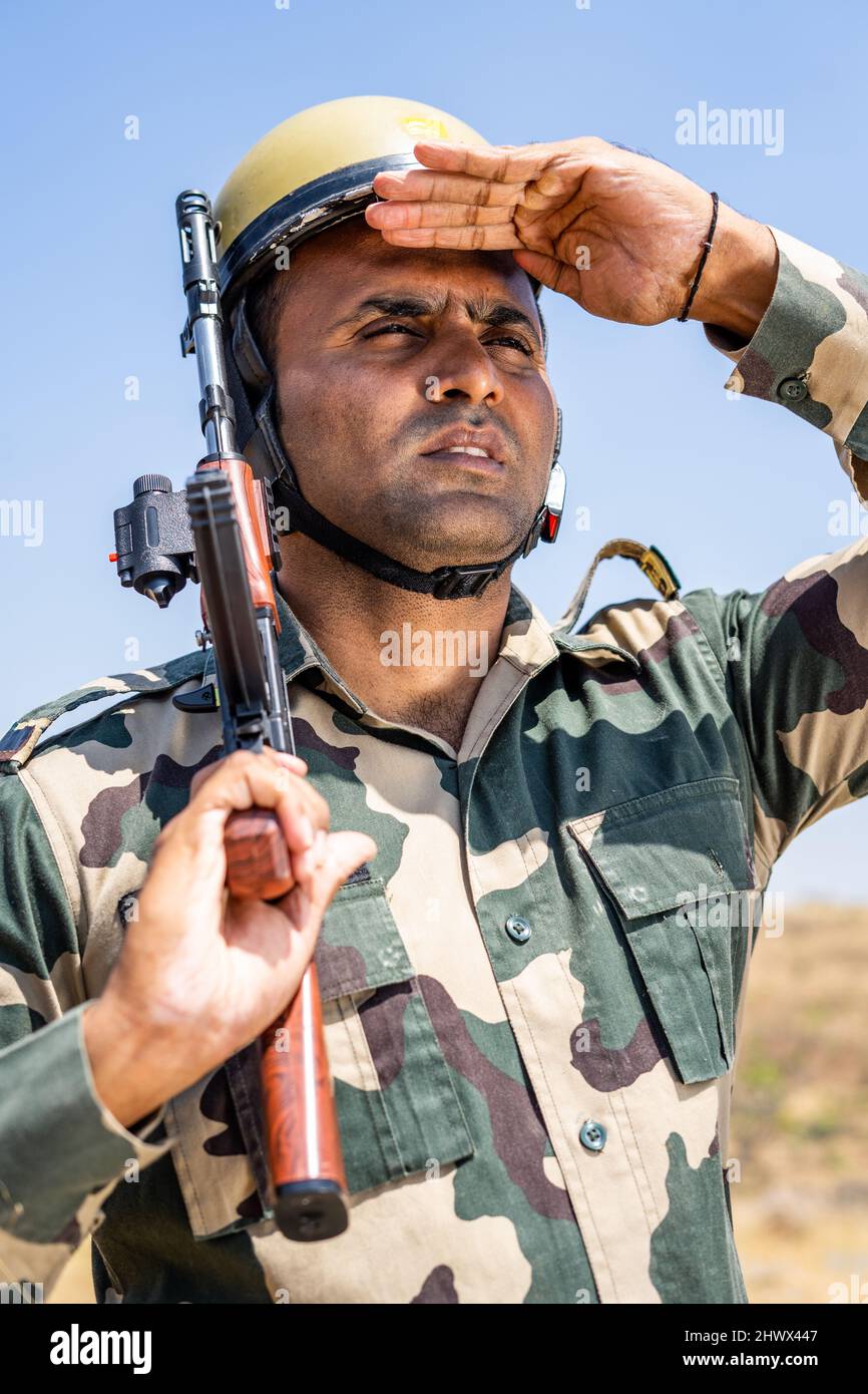 Soldato con mano di pistola che guarda intorno in cima alla collina con bandiera indiana volante sullo sfondo - concPET della forza di protezione di confine, serviceman in servizio e. Foto Stock