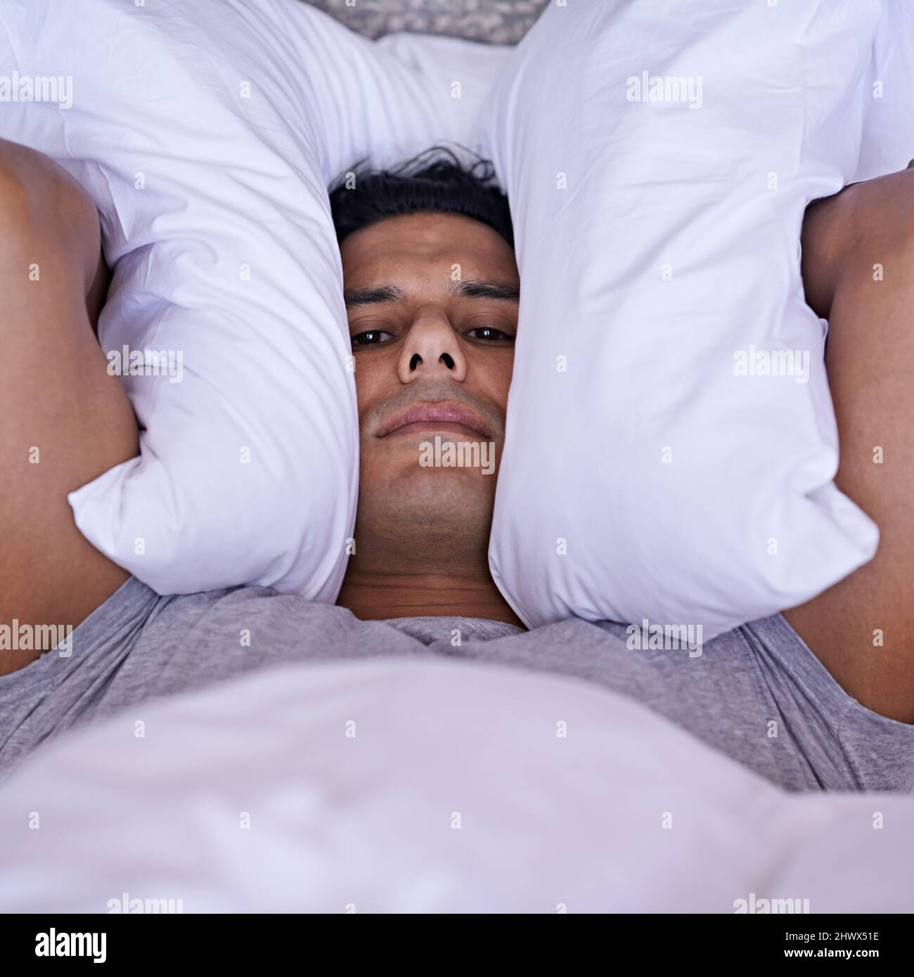 Nessuno può dormire con tutto questo rumore. Un giovane che gli copriva le orecchie con il cuscino. Foto Stock