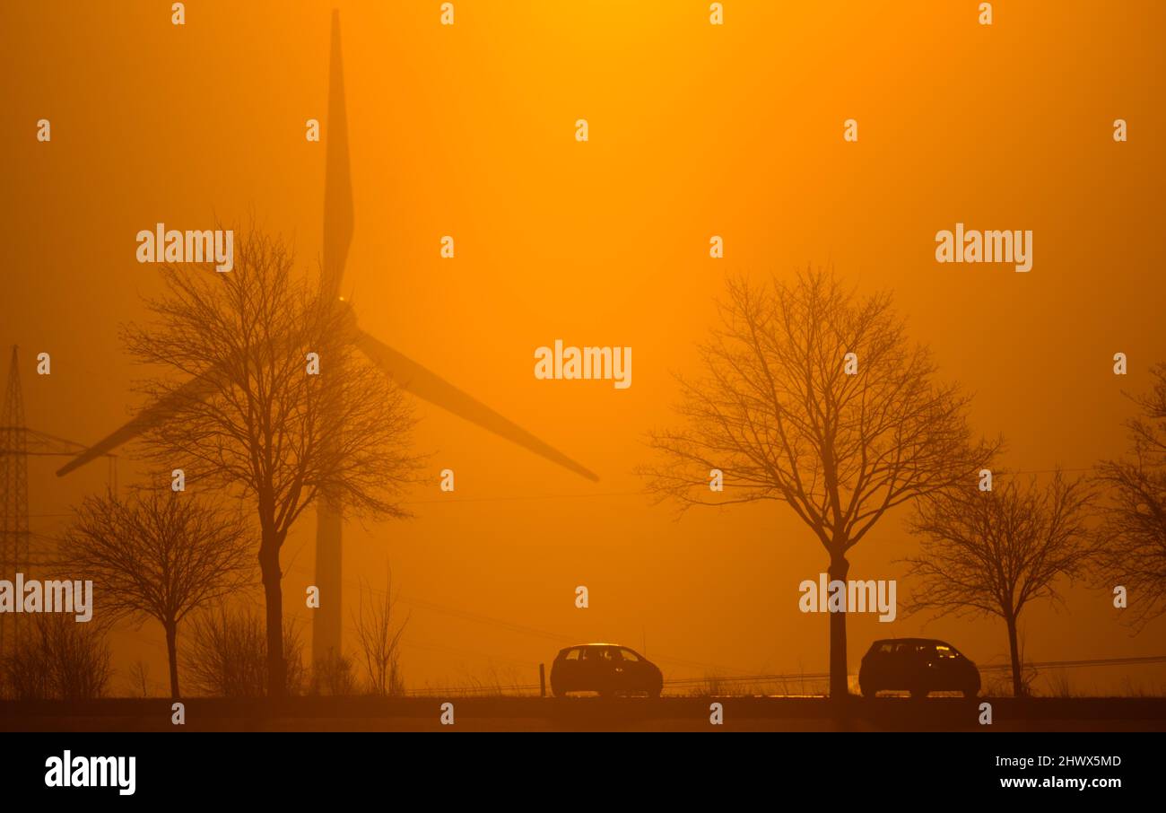 Laatzen, Germania. 08th Mar 2022. Le auto percorrono una strada di campagna nella regione di Hannover alla luce del sole nascente. Dietro di loro si può vedere una turbina eolica. In considerazione del drastico aumento dei prezzi dell'energia, il ministro dell'energia della bassa Sassonia (DOCUP) chiede un ulteriore aiuto ai cittadini. Credit: Julian Stratenschulte/dpa/Alamy Live News Foto Stock