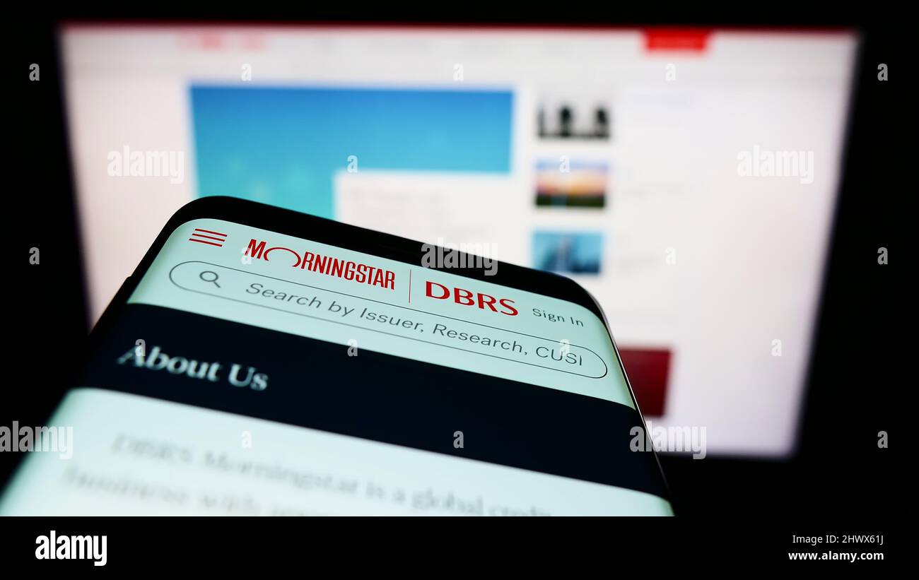Smartphone con sito web della società di rating canadese DBRS Morningstar sullo schermo di fronte al monitor. Mettere a fuoco sulla parte superiore sinistra del display del telefono. Foto Stock