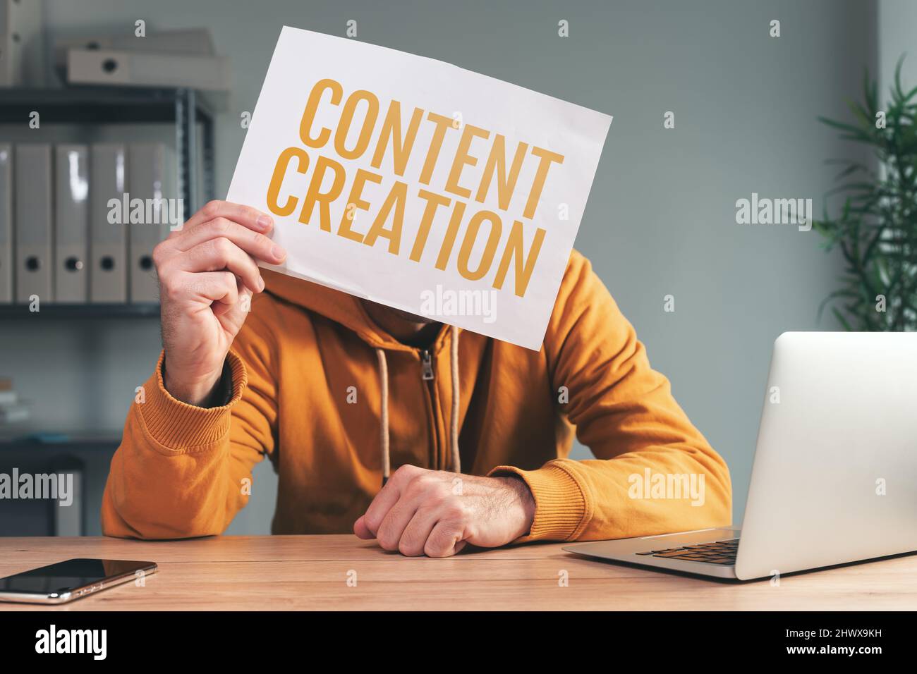 Creazione di contenuti, uomo che tiene la carta di fronte al suo volto in casa ufficio interno, fuoco selettivo Foto Stock