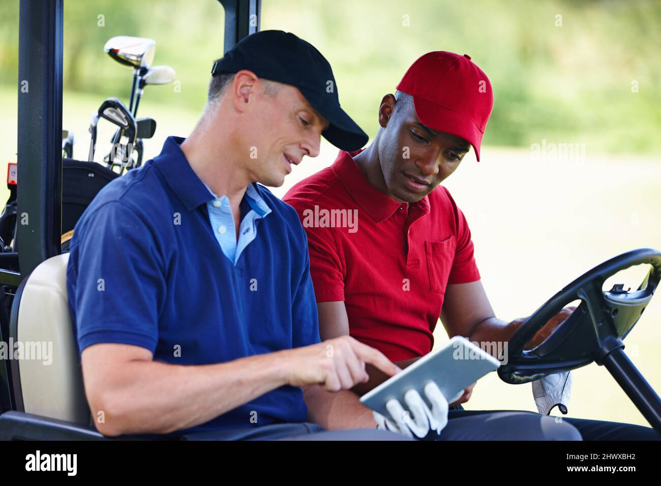 Ottenere i migliori consigli di golf online. Scatto di due uomini in un golf cart guardando un tablet digitale. Foto Stock