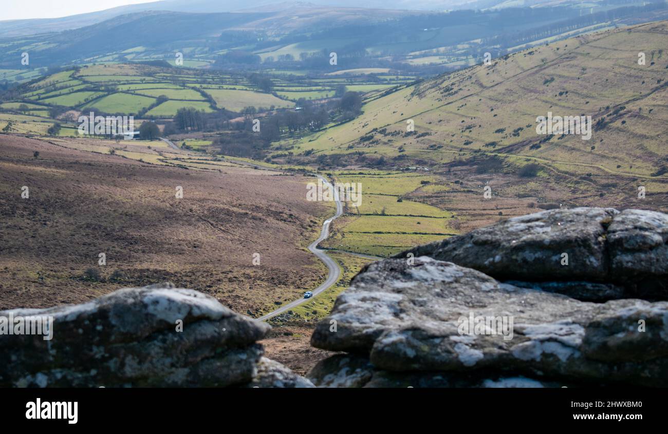 Una strada luminosa e tortuosa si snoda attraverso il parco nazionale di Dartmoor. Un morbido primo piano aggiunge un senso di scala quando la strada attraversa una valle Foto Stock