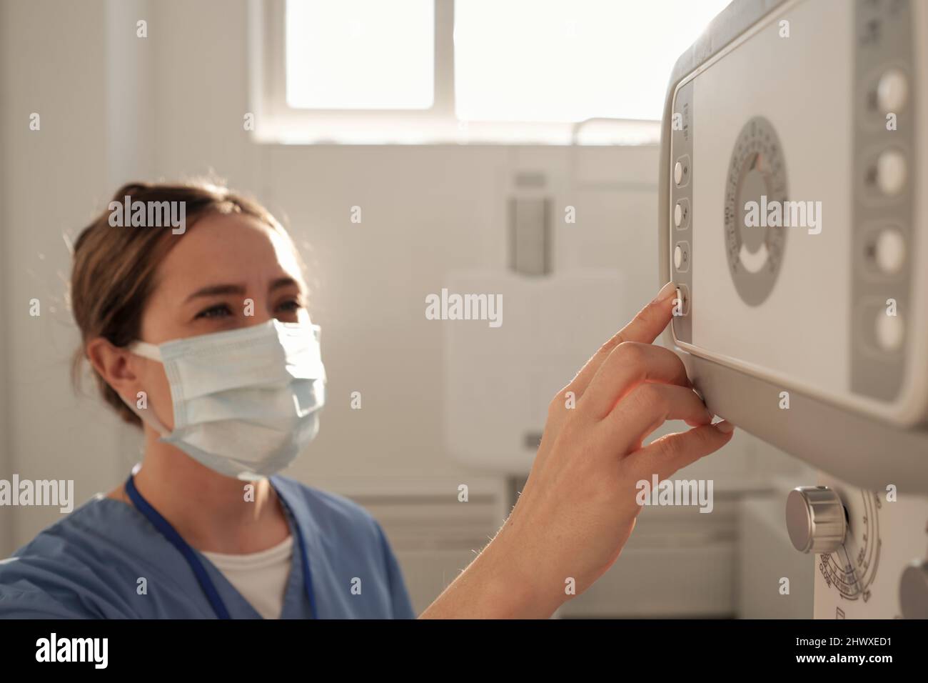 Giovane infermiere che preme il pulsante sul pannello di controllo dell'apparecchiatura a raggi X durante la preparazione all'esame radiologico dei pazienti Foto Stock