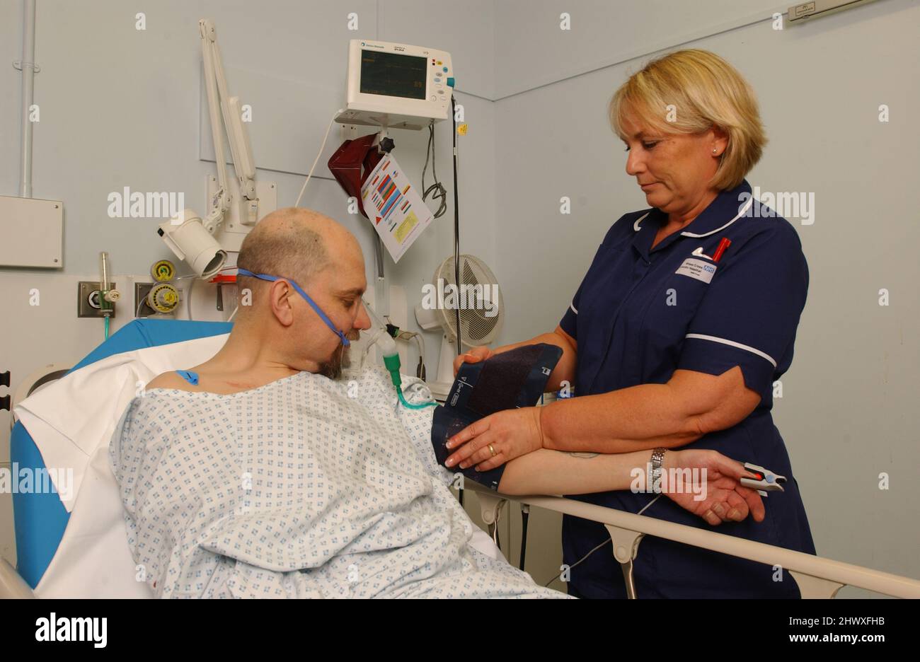 Un malato di attacco di cuore maschio si deposita nel suo letto con una riserva di ossigeno come un infermiere controlla la sua pressione sanguigna.(MODELLO RILASCIATO) Foto Stock
