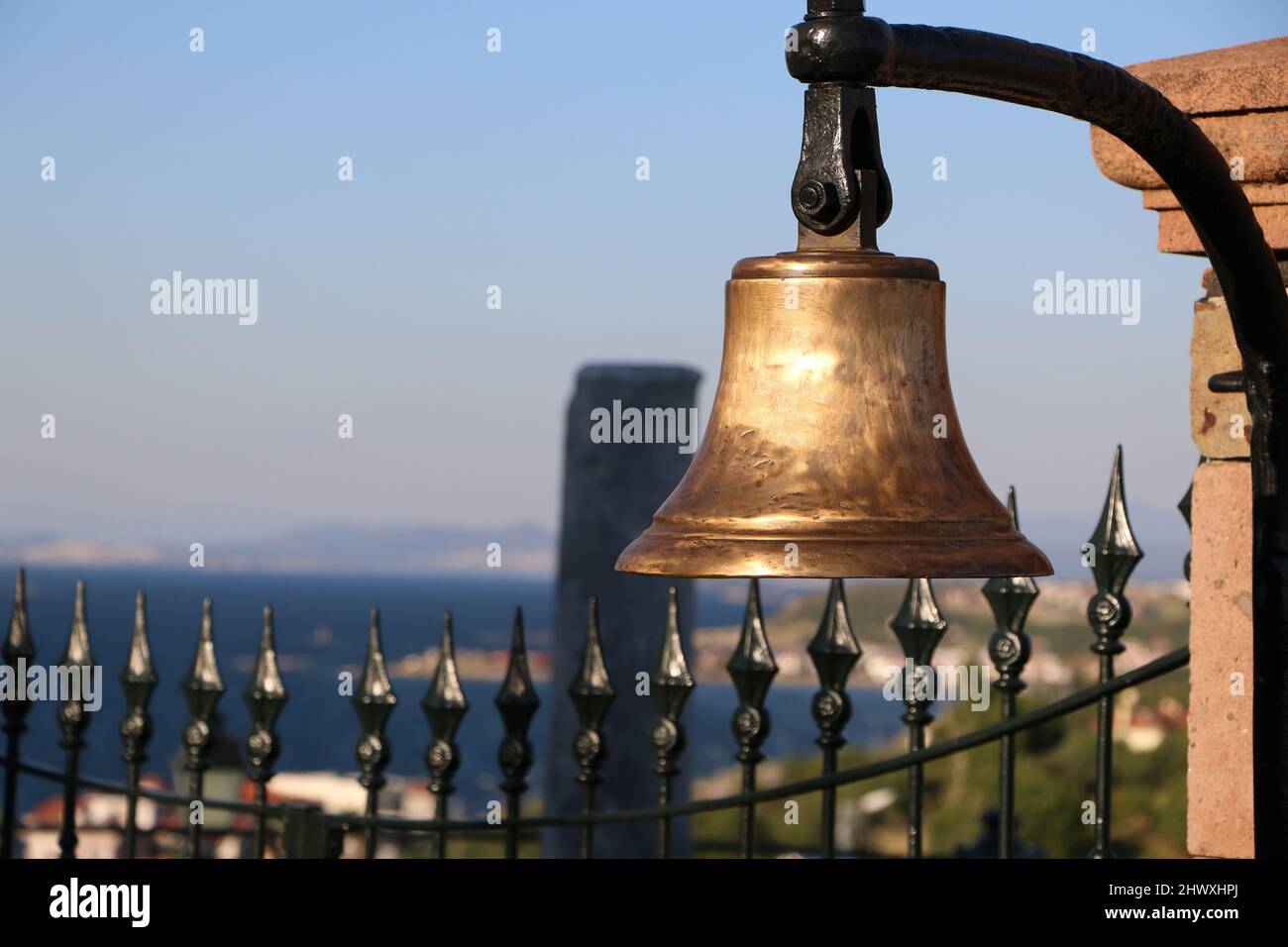 Vecchia campana di bronzo sul muro. Campana d'oro storica. Una campana e vista mare e paesaggio alle sue spalle. Campana della Chiesa. Foto Stock