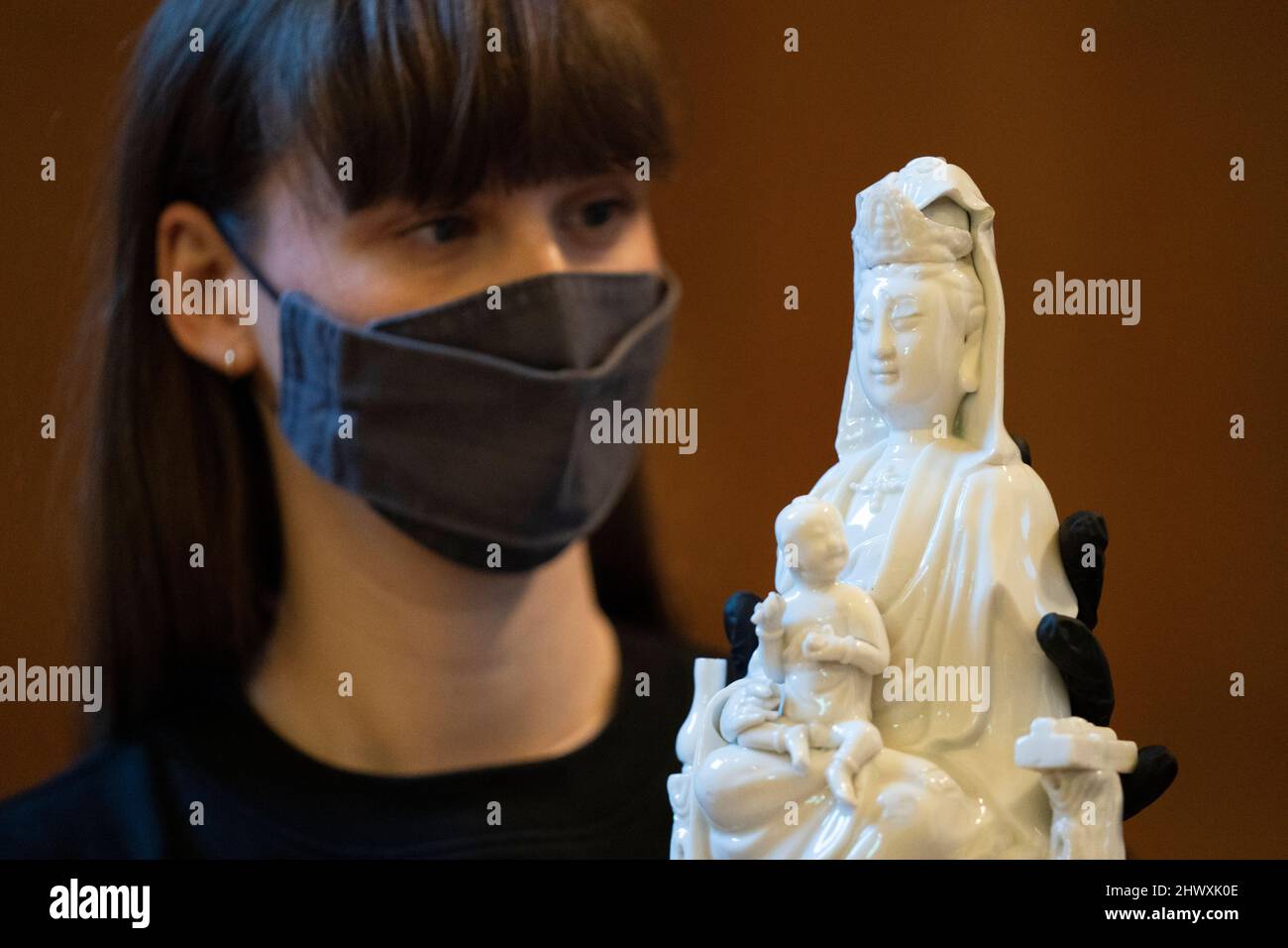 Un membro dello staff del British Museum guarda una figura in porcellana di Guanyin con bambini e assistenti, provenienti dalla Cina, 18th secolo, durante il lancio della mostra Citi Feminine Power: Il divino al demoniaco, nella Giornata Internazionale della Donna al British Museum di Londra, per la presentazione di un'icona della dea indù Kali recentemente acquisita dall'artista bengalese, Kaushik Ghosh. Data foto: Martedì 8 marzo 2022. Foto Stock