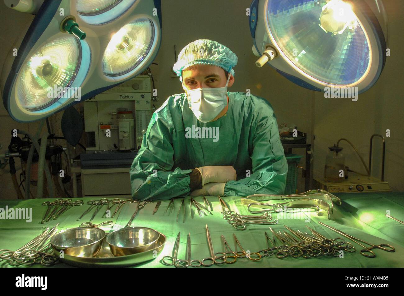 Un chirurgo mascherato si appoggia su una fila di strumenti chirurgici sterili in un teatro ospedaliero (MODELLO RILASCIATO) Foto Stock