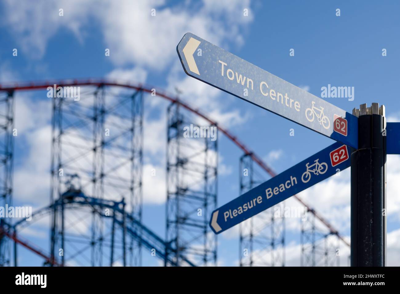 Un segnale di direzione che indica la strada per Pleasure Beach e il centro città di Blackpool, Lancashire, Regno Unito. Le montagne russe "Big One" sono sullo sfondo Foto Stock