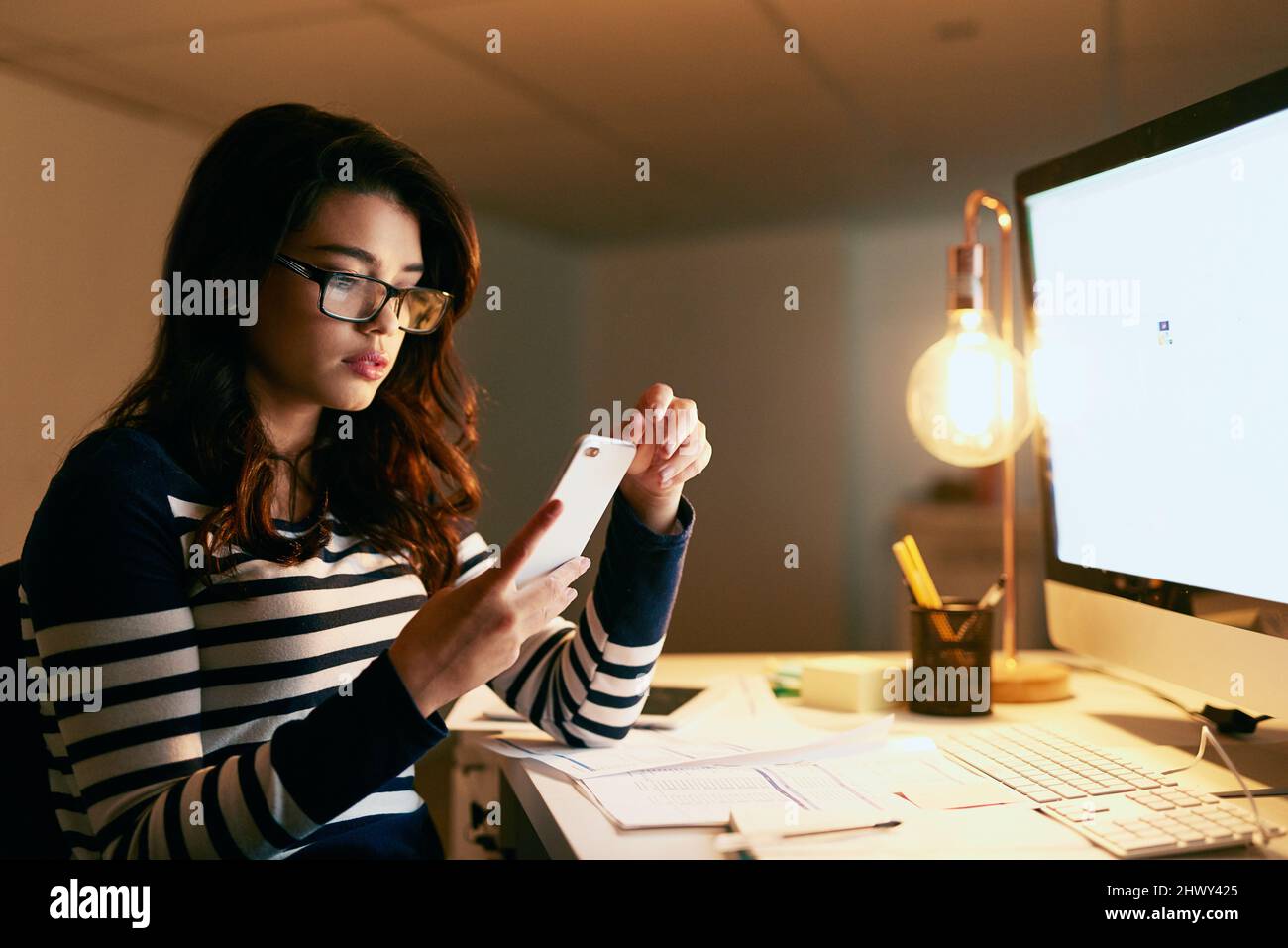Non aspettarmi, mi sta lavorando tardi. Scatto di una giovane donna d'affari che texting sul suo cellulare mentre lavora tardi in un ufficio. Foto Stock