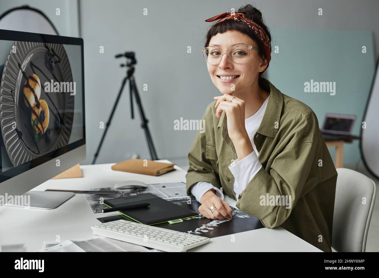 Ritratto di giovane fotografo femminile che guarda la fotocamera mentre si siede sul posto di lavoro in studio fotografico Foto Stock