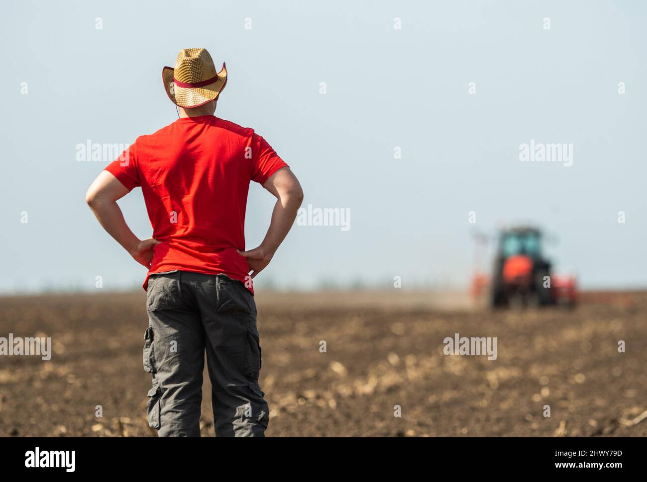 Giovane agricoltore su terreni agricoli con trattore in background Foto Stock