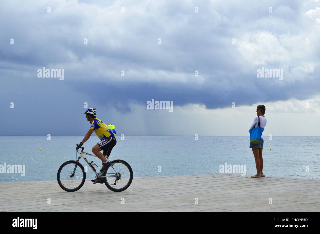 Persone sul sentiero lastricato vicino alla spiaggia di Barceloneta, le nuvole tempestose che si avvicinano alla costa di Barcellona Spagna. Foto Stock