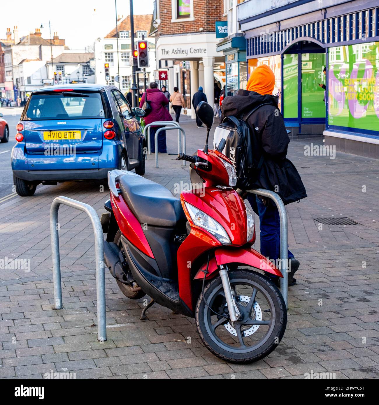 Epsom Surrey London UK, marzo 8 2022, Man Standing accanto A un Red Motor Scooter parcheggiato su un marciapiede Foto Stock