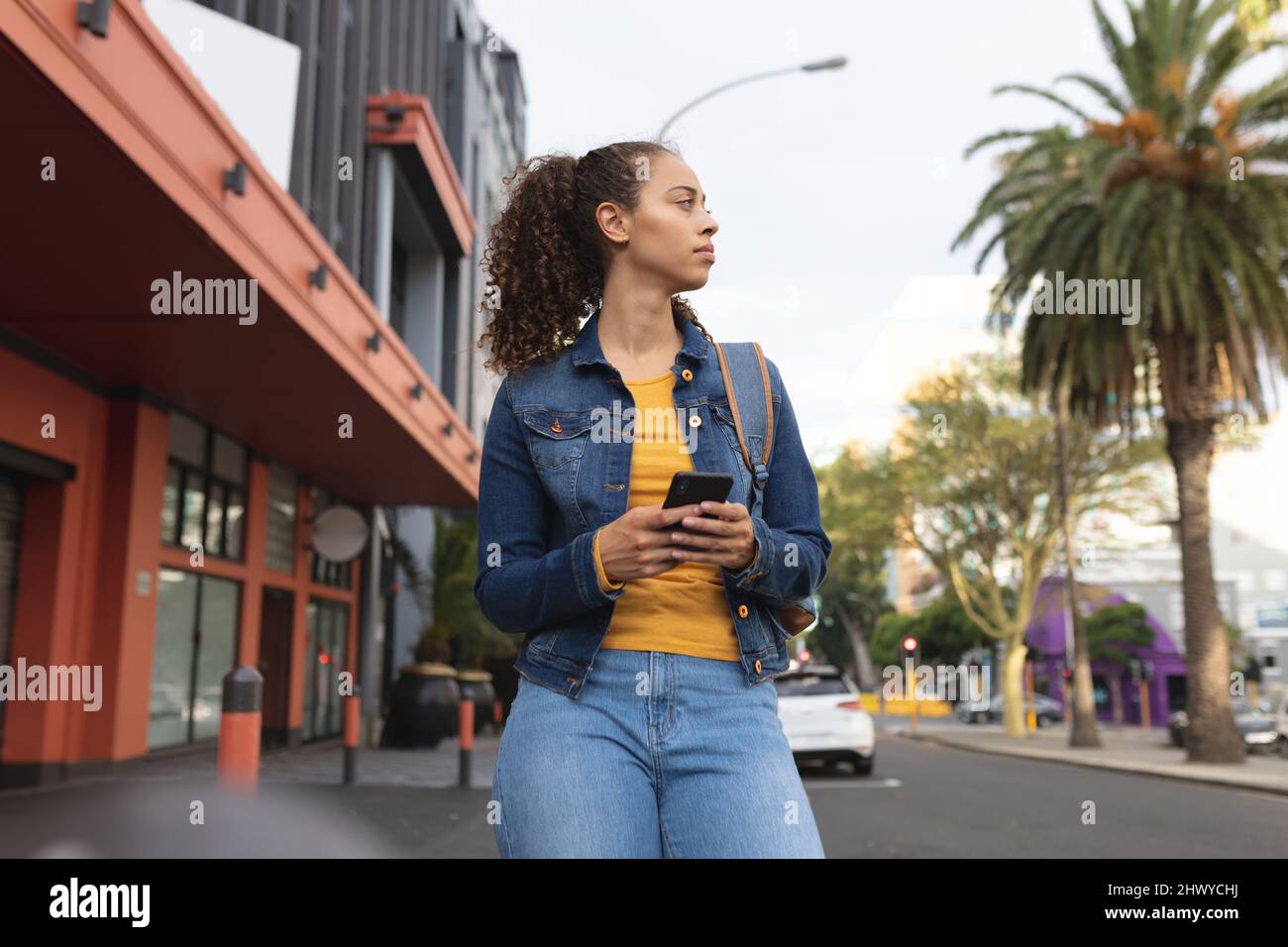 Giovane afroamericana con smartphone che guarda via in città Foto Stock