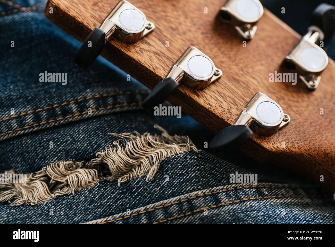 Il collo della chitarra acustica è in primo piano sul tessuto in denim. Cultura hipster. Sfondo. Strumento musicale. Imparare a suonare la chitarra. Foto Stock