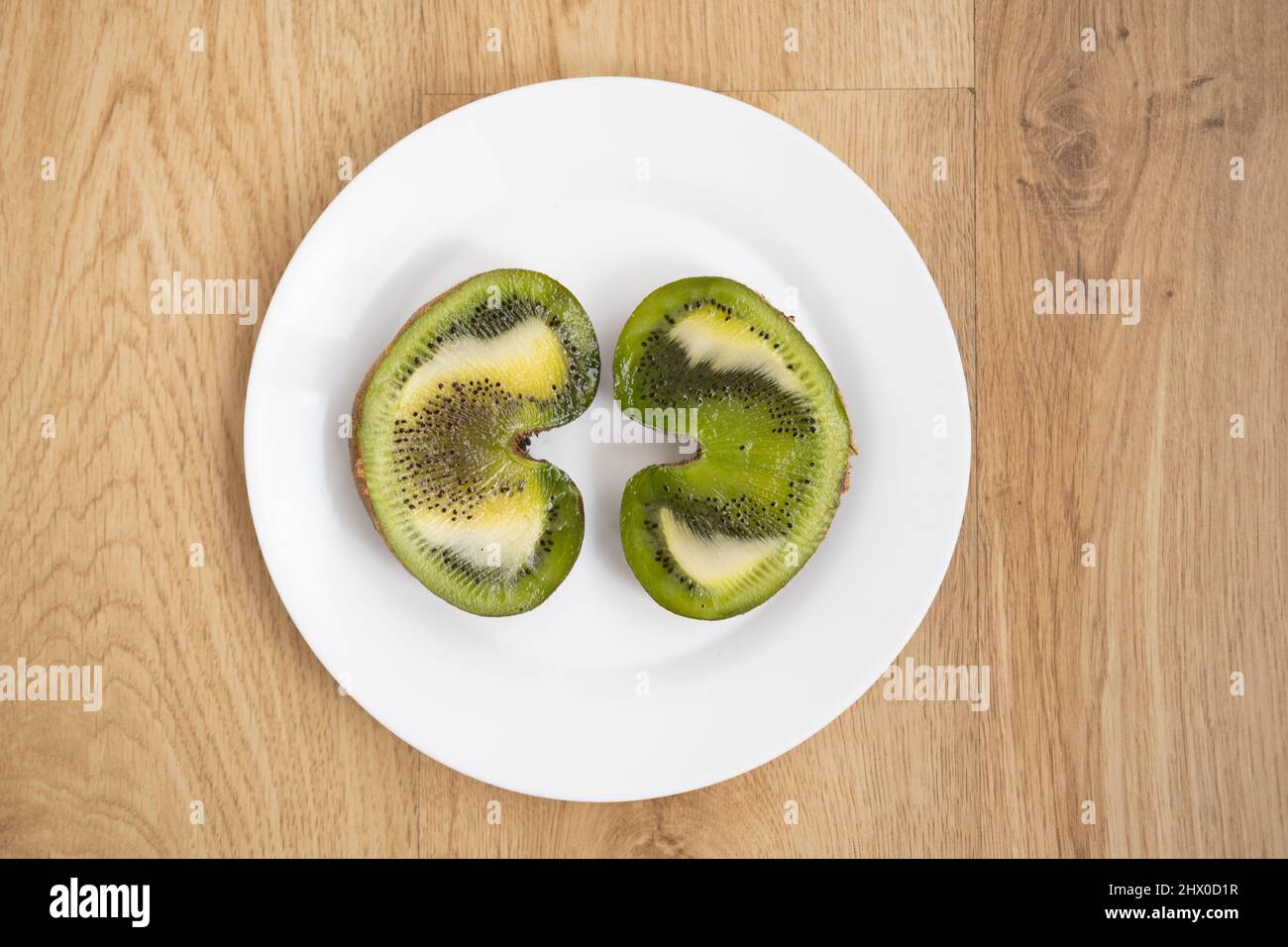 Immagine piatta di due metà di un kiwi a forma di cuore su un piatto bianco su una superficie di legno Foto Stock