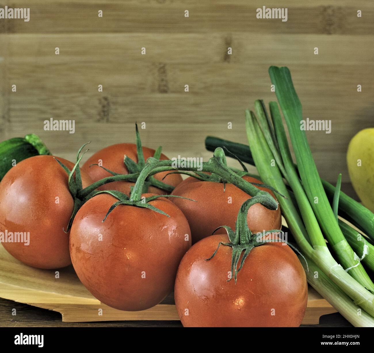 Cinque pomodori su un vitigno con cipolle verdi su sfondo di tavola di legno. Foto Stock