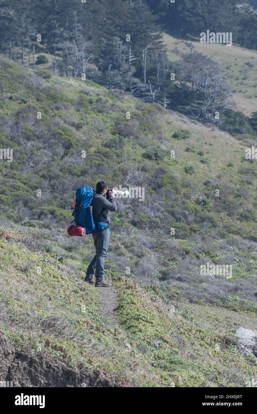 Un zaino in spalla in un trekking ferma per scattare foto con un teleobiettivo lungo il sentiero Lost Coast nella contea di Humboldt, California del Nord, Stati Uniti. Foto Stock