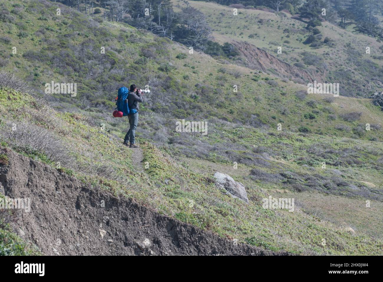 Un zaino in spalla in un trekking ferma per scattare foto con un teleobiettivo lungo il sentiero Lost Coast nella contea di Humboldt, California del Nord, Stati Uniti. Foto Stock