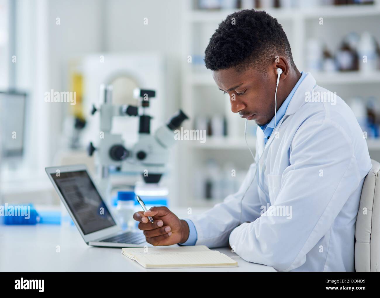 La ricerca non ha sostituti. Scatto corto di un giovane scienziato maschile concentrato che lavora sul suo computer portatile mentre si siede all'interno di un laboratorio. Foto Stock