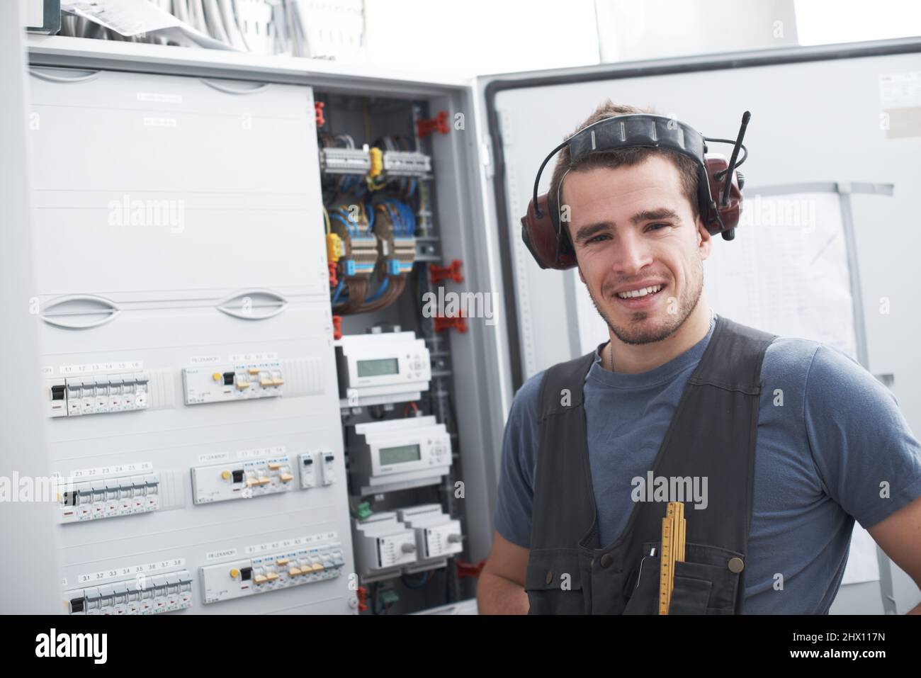 La sua esperienza elettrica farà il lavoro. Giovane appaltatore accanto a un quadro di distribuzione elettrica. Foto Stock