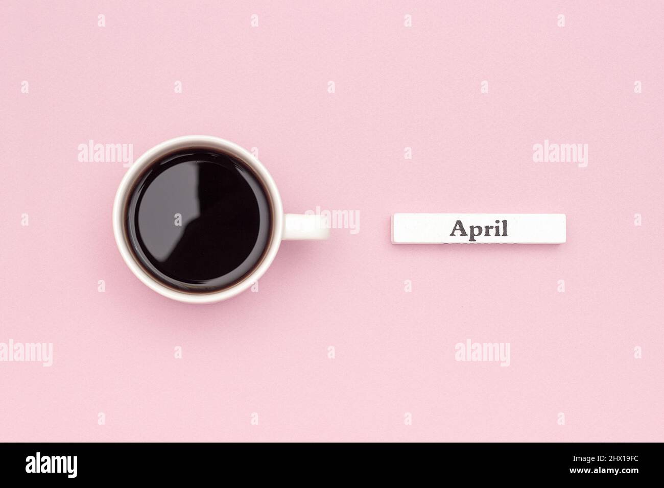 Calendario in legno mese di primavera aprile e tazza di caffè nero su sfondo di carta rosa pastello. Concept Hello April Creative Top View Flat Lay Greeting ca Foto Stock