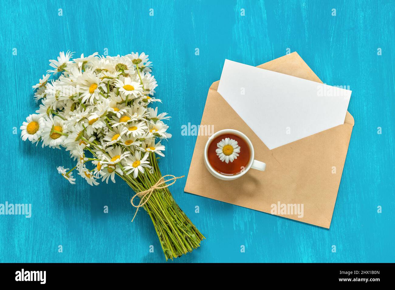 Bouquet camomiles bianco fiori tazza di erbe tè e lettera busta artigianale su sfondo blu rustico concetto vintage buona mattina Estate tè tempo GRE Foto Stock
