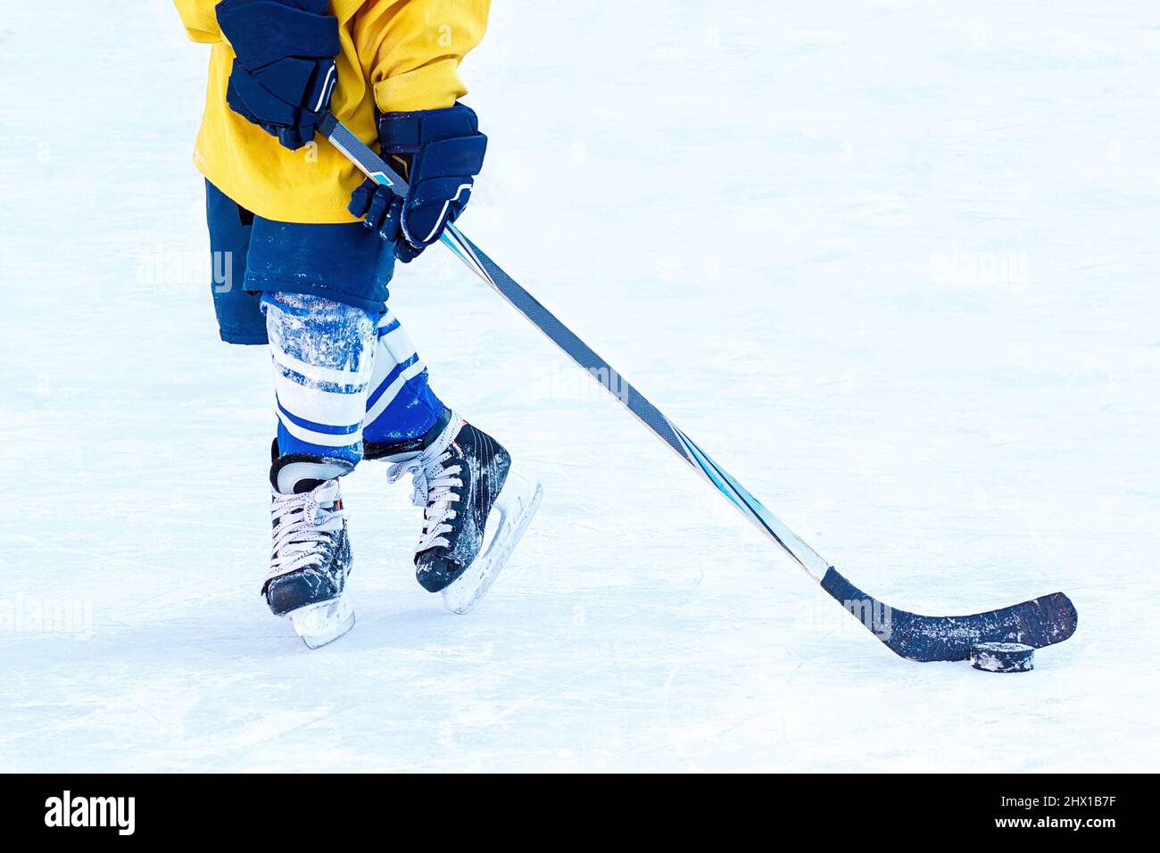 Piedi di un giovane giocatore di hockey, bastone di hockey e puck primo piano sullo sfondo del ghiaccio. Foto Stock