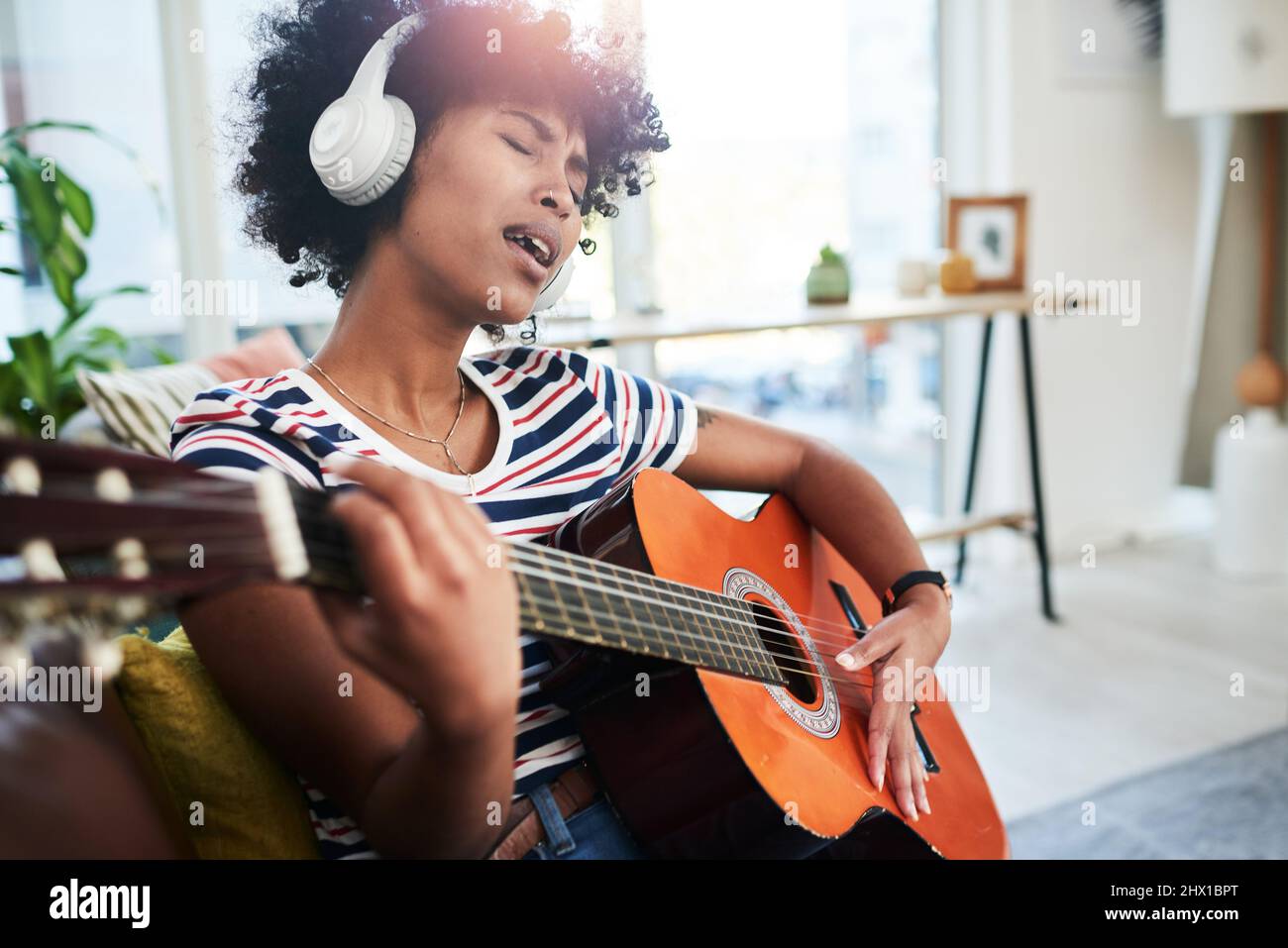 La musica è un succhietto naturale. Scatto di una donna che indossa le cuffie mentre suona la chitarra a casa. Foto Stock