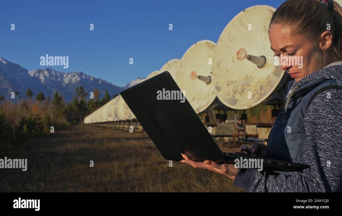 Donna studente operatore di Istituto di fisica solare terrestre monitora le apparecchiature di comunicazione in notebook. Cannocchiale radio solare a schiera unico. Sun Solar radio Telescope. L'osservatorio 'Quasar' a Badary, Russia. Piatti satellitari in montagna. Foto Stock