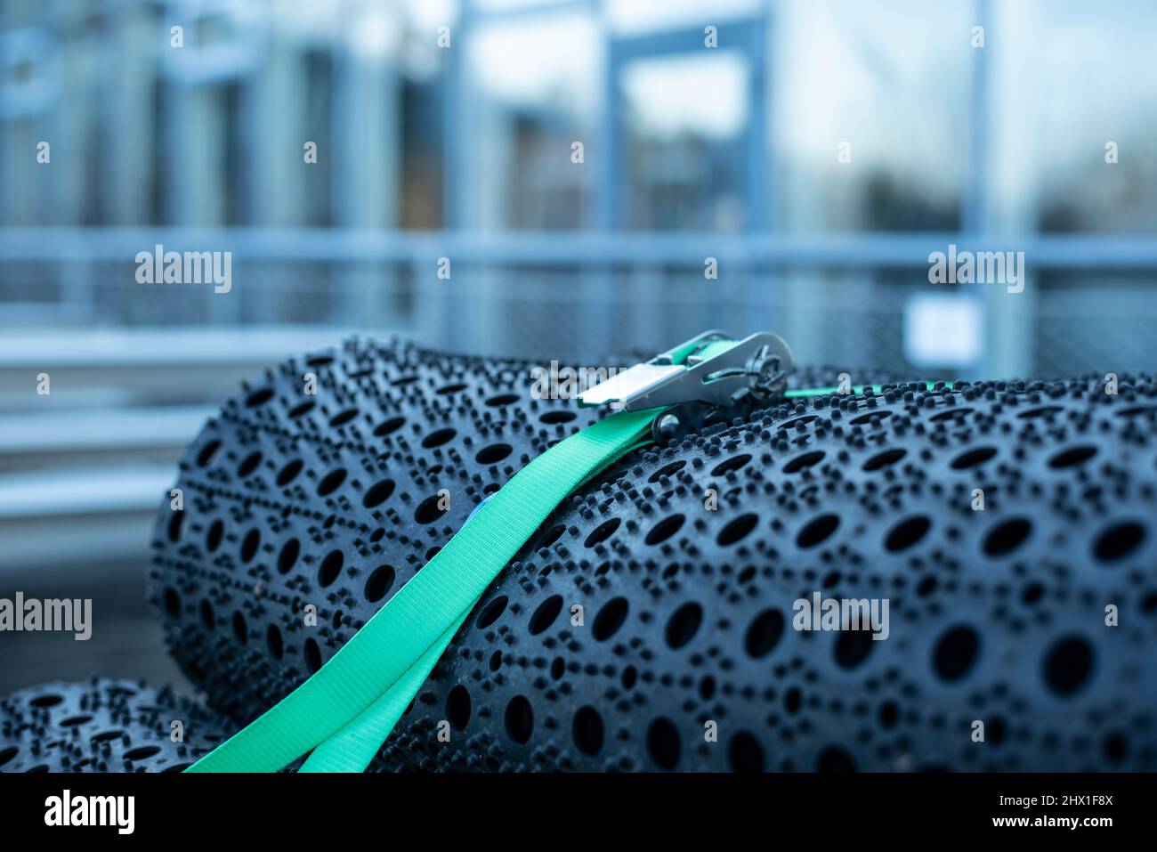 una cintura di fissaggio verde tiene insieme un mucchio di tappetini neri in gomma per esterni Foto Stock