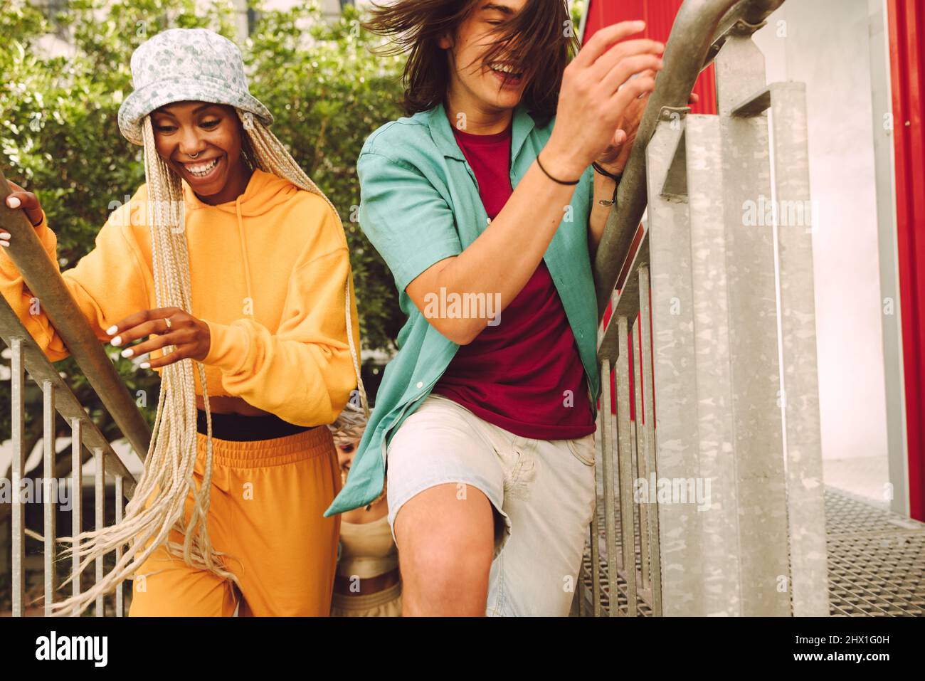 Giovani amici felici che corrono sulle scale all'aperto. Gruppo di giovani allegri sorridenti e che si divertono insieme. Amici multietnici che hanno Foto Stock