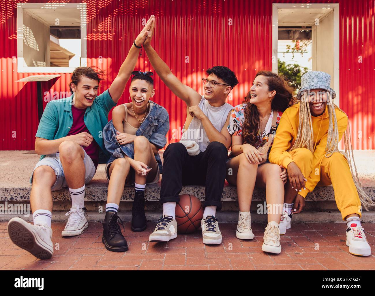Ecco all'amicizia. Gruppo di giovani multietnici che si divertono a stare insieme all'aria aperta della città. Allegri amici di generazione z divertirsi a Foto Stock