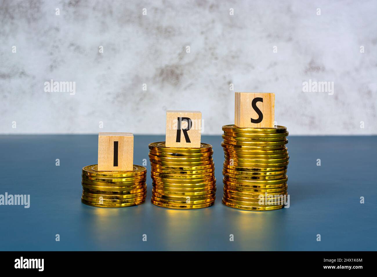 Testo IRS su cubo di legno con monete d'oro su sfondo blu. Concetto aziendale e fiscale. Foto Stock