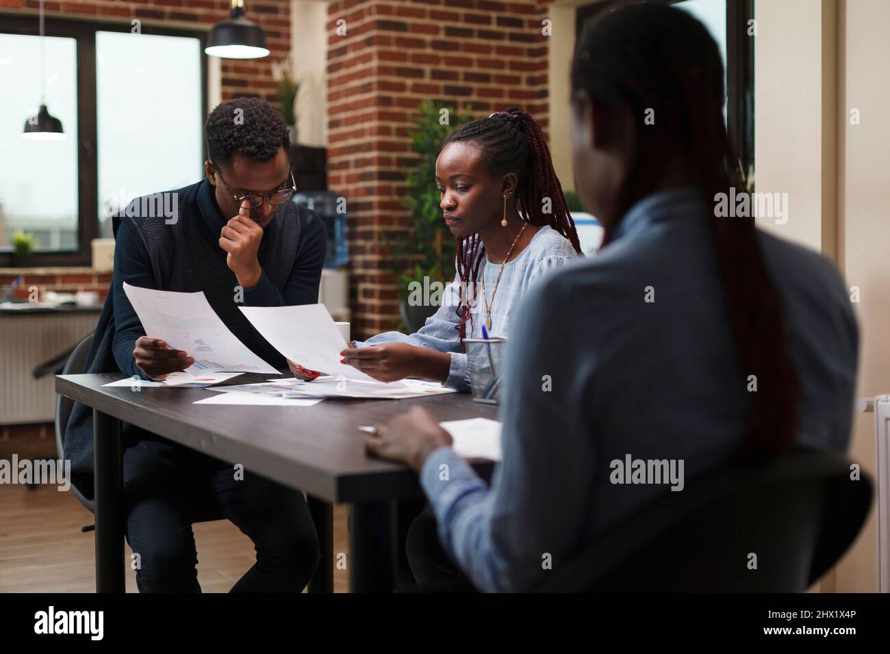 I membri del team delle agenzie di marketing esaminano la documentazione contabile e i dati statistici sui ricavi. I colleghi della società di affari afro-americana nell'incontro circa lo stato finanziario di progetto di startup. Foto Stock
