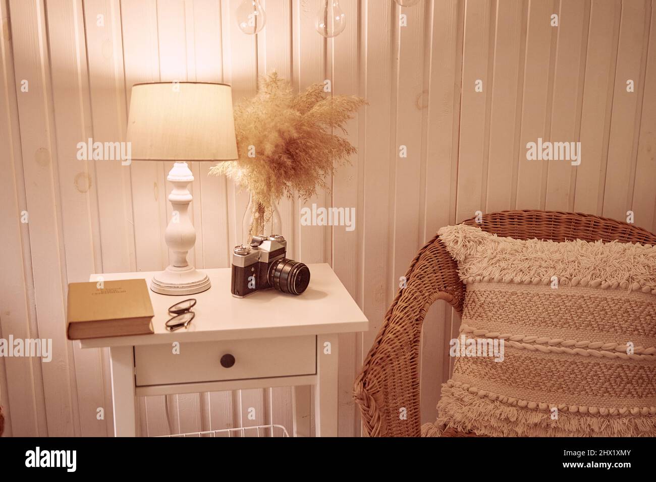 Interni in stile bohémien con un'accogliente atmosfera serale. Casa accogliente, confortevole con arredamento a secco canne, vecchia macchina fotografica, libro vintage e lampada da tavolo. Interno estetico Foto Stock