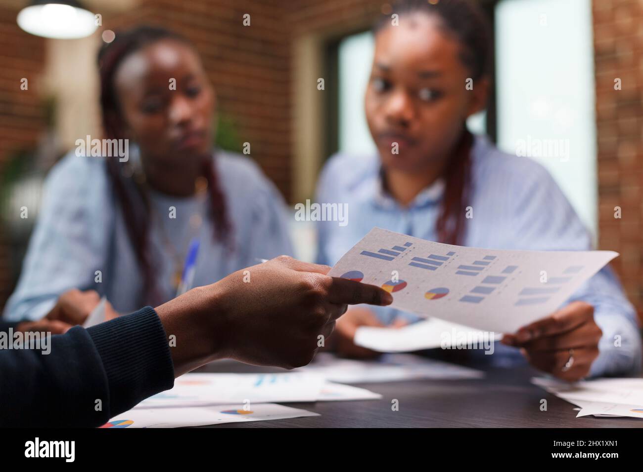 Focalizzazione selettiva della mano del dipendente che ha un grafico di gestione durante l'incontro con i colleghi. Colleghi aziendali che esaminano i piani finanziari aziendali e la documentazione contabile. Foto Stock