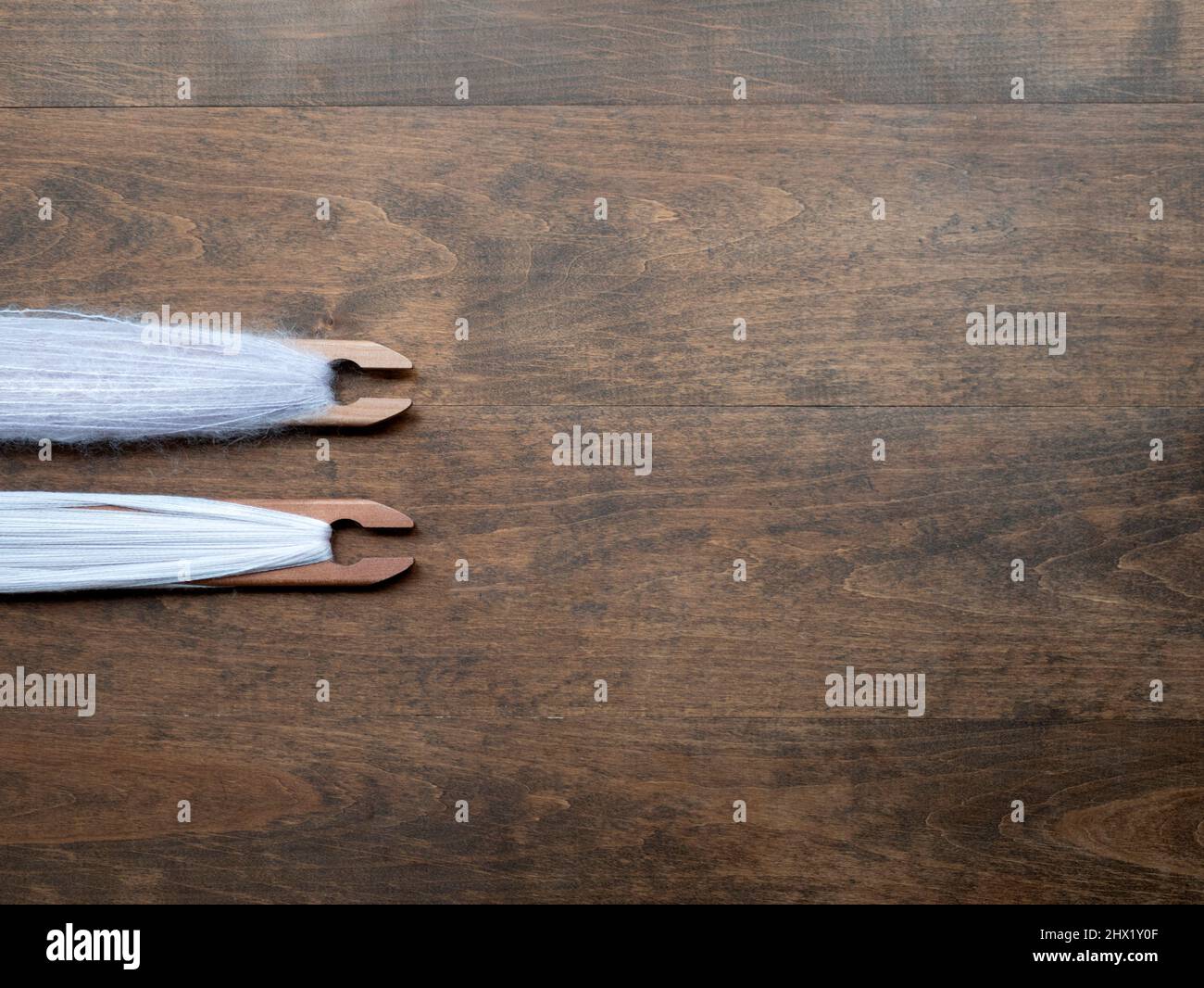 Sfondo di legno marrone con due navette tessenti piene di filo rosa chiaro, spazio copia. Concetto di artigianato, tessitura, lavorazione tessile Foto Stock