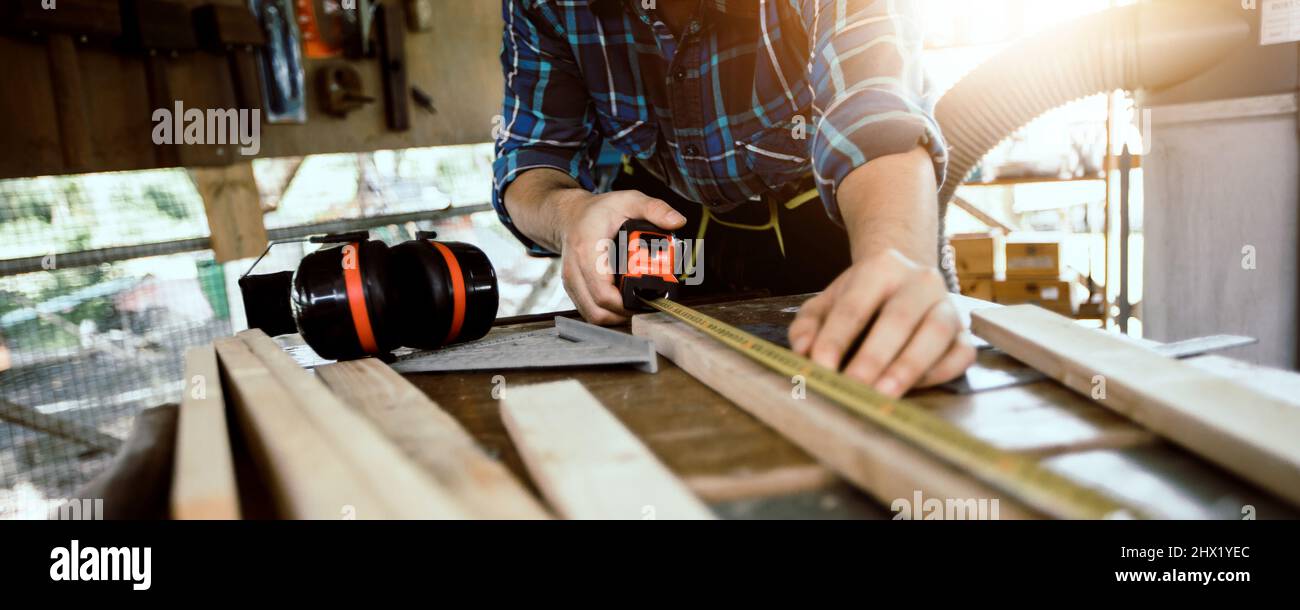 Il carpentiere misura con un metro a nastro sul banco di lavoro. Il concetto di lavorazione del legno e dei mobili in officina contrassegna e assembla parti del mobile Foto Stock