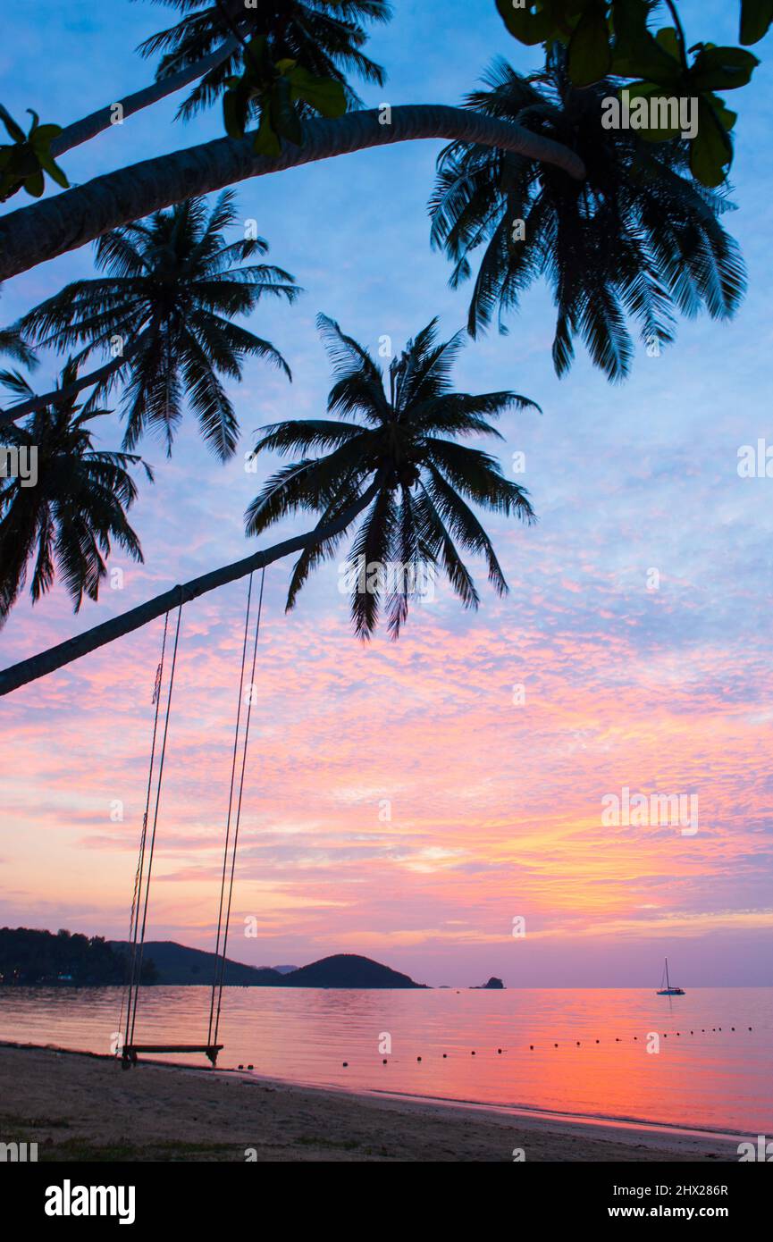 Una tranquilla spiaggia tropicale al tramonto, le spettacolari nuvole nel colorato cielo del tramonto, swing appeso sulle palme da cocco. Trat, Tailandia. Foto Stock
