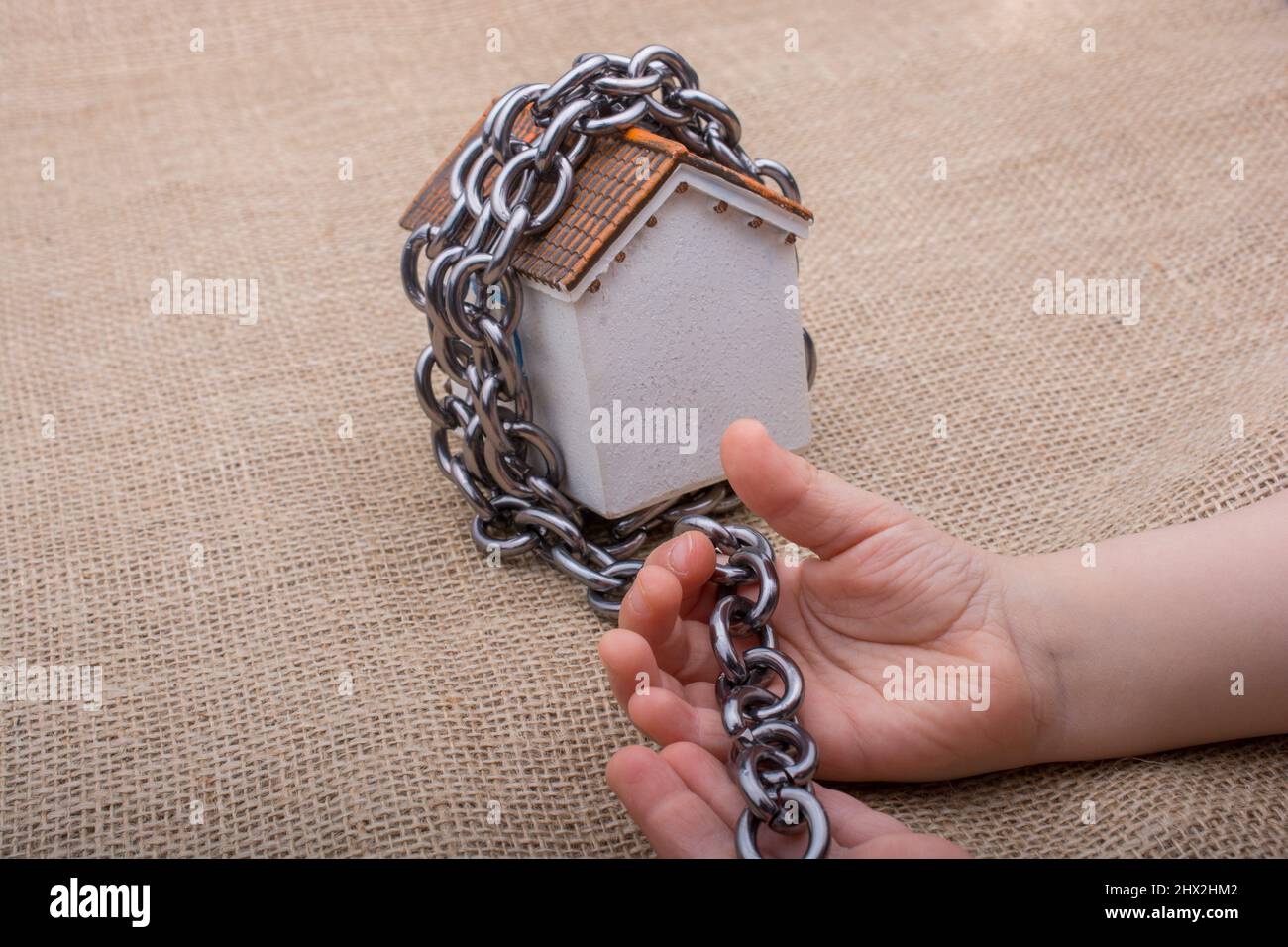 Piccola mano che tiene una catena intorno ad una casa modello su uno sfondo marrone. Foto Stock