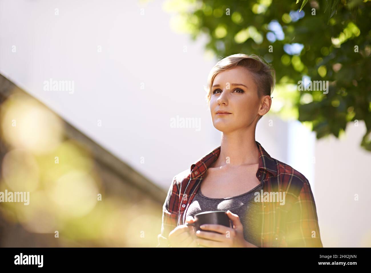 Mi piace fare delle pause all'aperto. Un taglio corto di una bella giovane donna che beve caffè nel suo giardino. Foto Stock