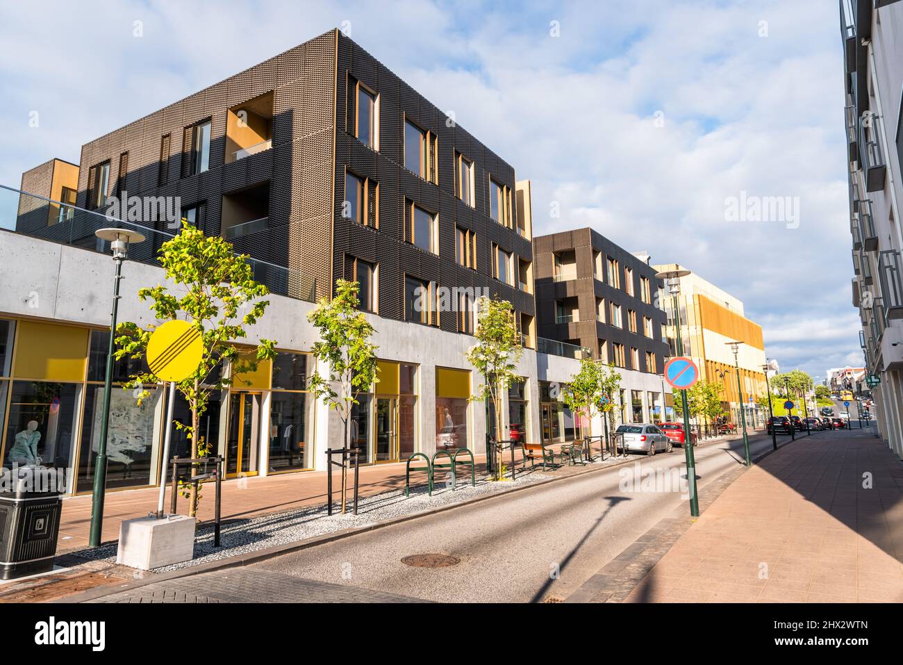 Moderni edifici residenziali con negozi al piano terra lungo una strada a senso unico nel centro della città in una giornata estiva soleggiata Foto Stock