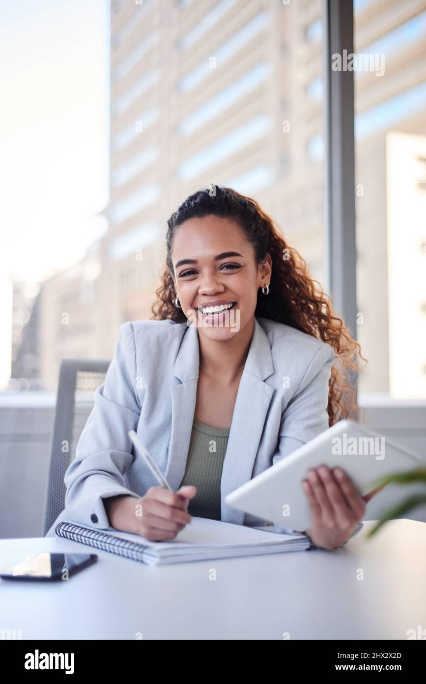 Un ritratto di giovane donna in ufficio in città sorridendo con un tablet e un notebook Foto Stock