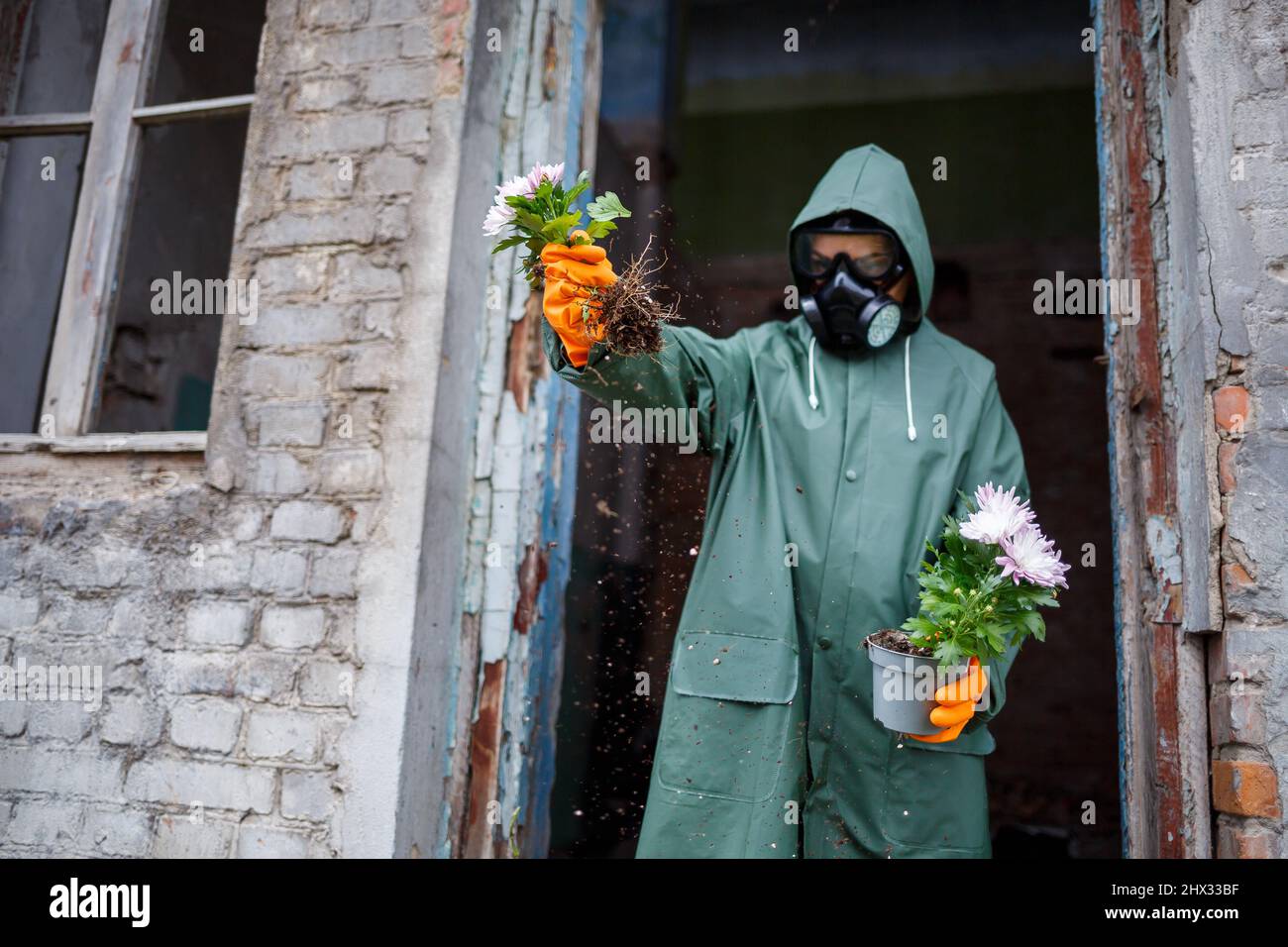 Uno scienziato dosimetristo in indumenti protettivi e una maschera a gas esamina la zona di pericolo. Primo piano. Fiore nelle mani Foto Stock