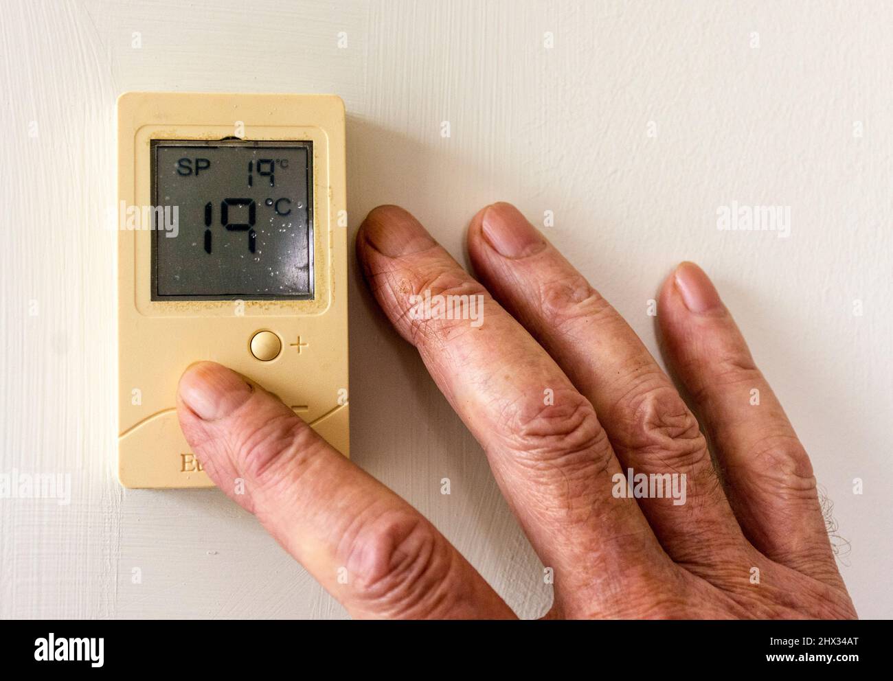 L'anziano, l'anziano, l'anziano regola la temperatura della sua casa su un termostato digitale man mano che i costi di riscaldamento salendo. Foto Stock