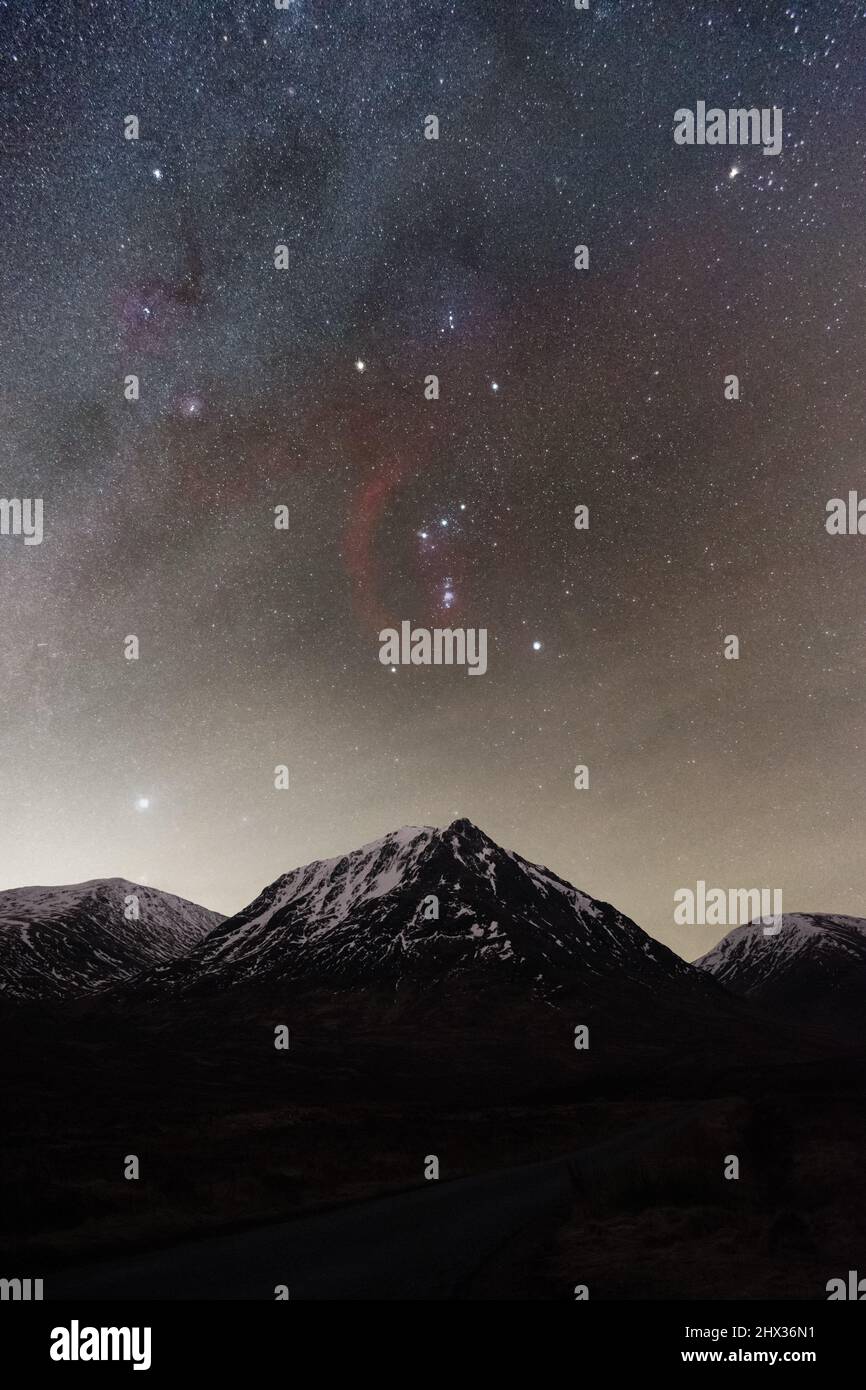 Orion e la Via Lattea che si innalzano sopra le vette innevate della montagna in Scozia Foto Stock