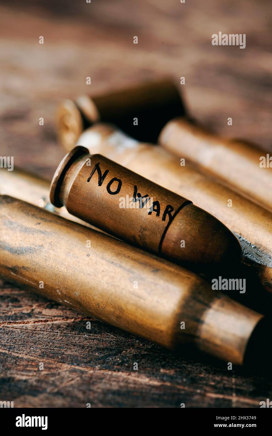 primo piano di una pallottola, con il testo senza guerra scritto a mano in essa, sopra un mazzo di proiettili usati, su una superficie rustica Foto Stock
