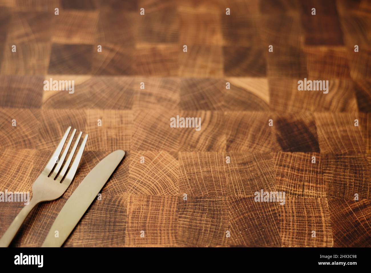 Una forchetta d'oro da pranzo e un coltello seduti in cima a un piano di un macellaio vuoto in una cucina Foto Stock